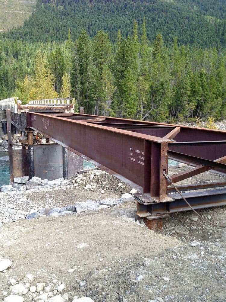 Vertical shot of bridge girder resting on concrete abutment and new pilings at Elk River, BC, with forested backdrop.