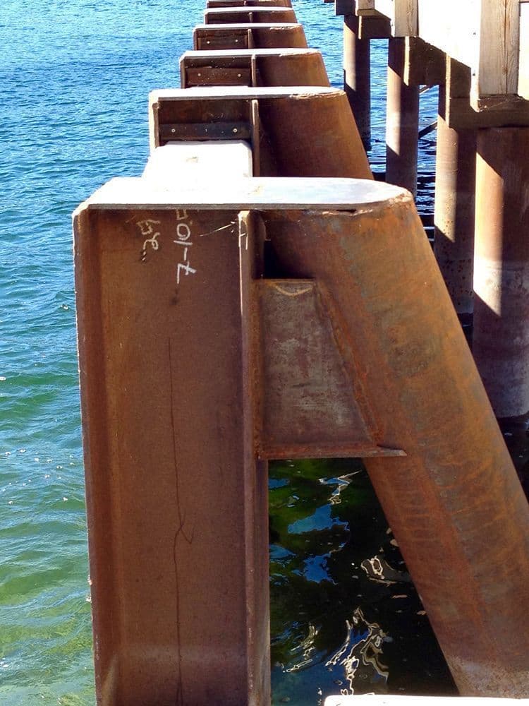 Close-up of metal railing and concrete edge of the OK Centre breakwater over clear green-blue lake water.
