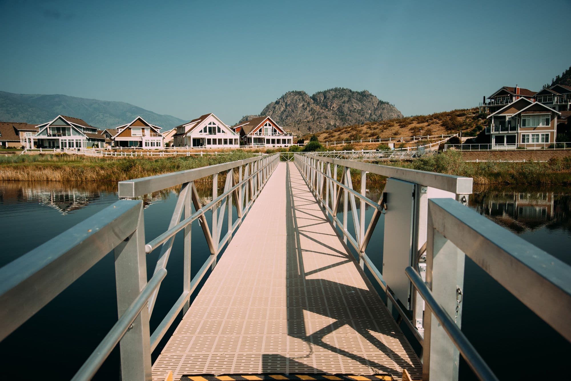 Pedestrian walkway at Osoyoos Cottages Marina with railing and mountain views, providing direct access to commercial dock slips.