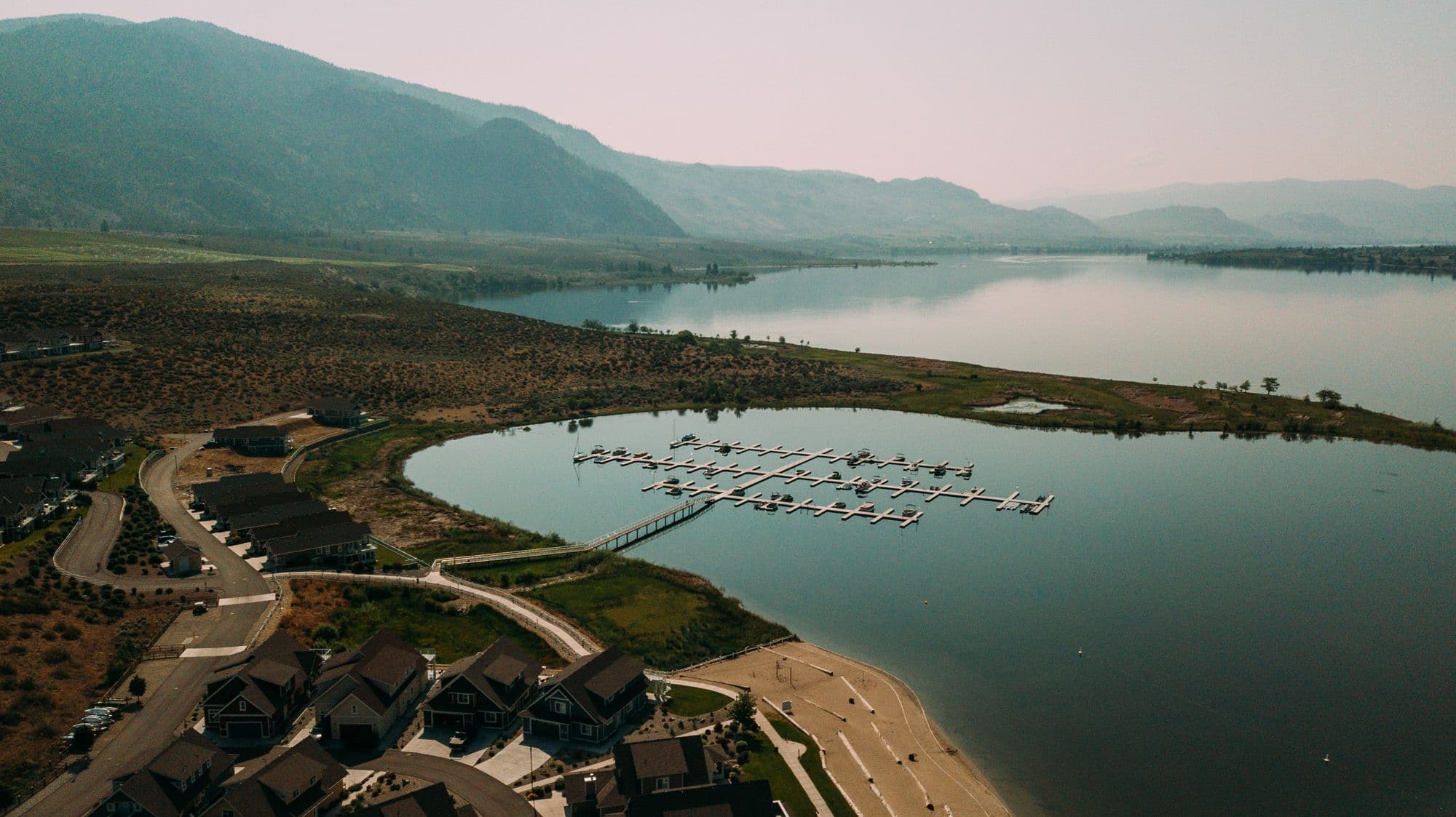 Wide aerial shot of the Osoyoos Cottages shoreline and marina basin, showing scale and layout of the full dock installation.
