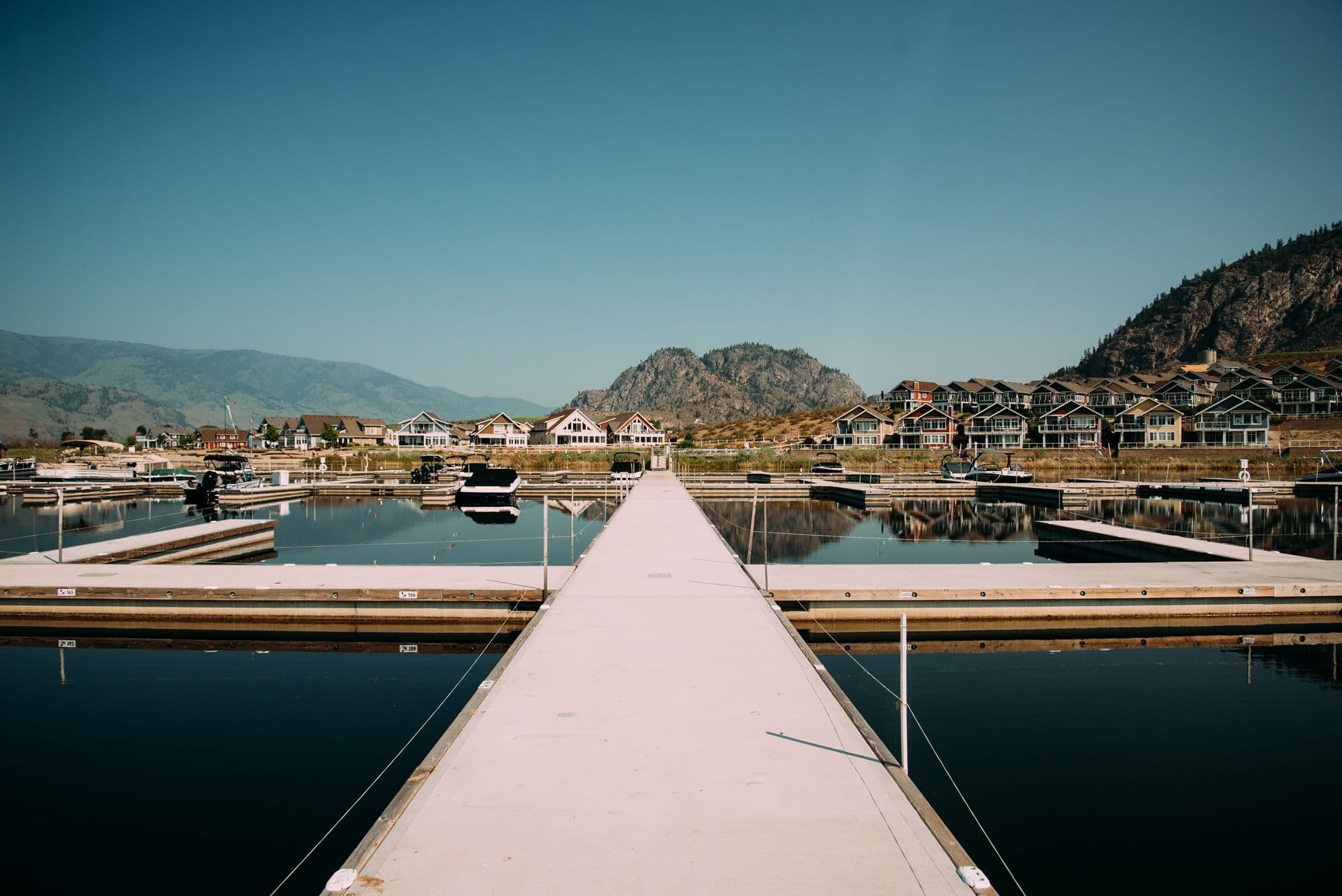 Centered dock approach at Osoyoos Cottages Marina showcasing clean layout and symmetry with mountain backdrop and protected waters.