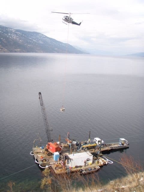 A helicopter lowers a load of materials onto a barge equipped with a crane and construction equipment during an underwater concrete anchoring operation for Sheerwater Marina on Kalamalka Lake in Kelowna, BC.