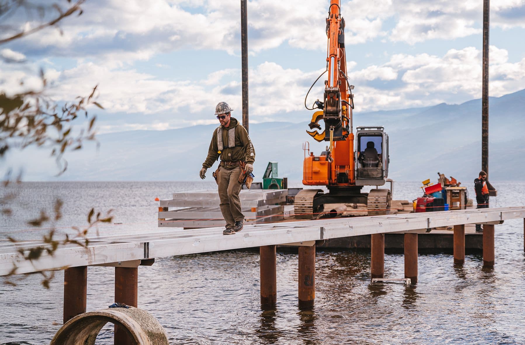 Burton Marine crew member walking on newly framed dock beside barge and excavator on Okanagan Lake, highlighting safe, professional dock construction services.