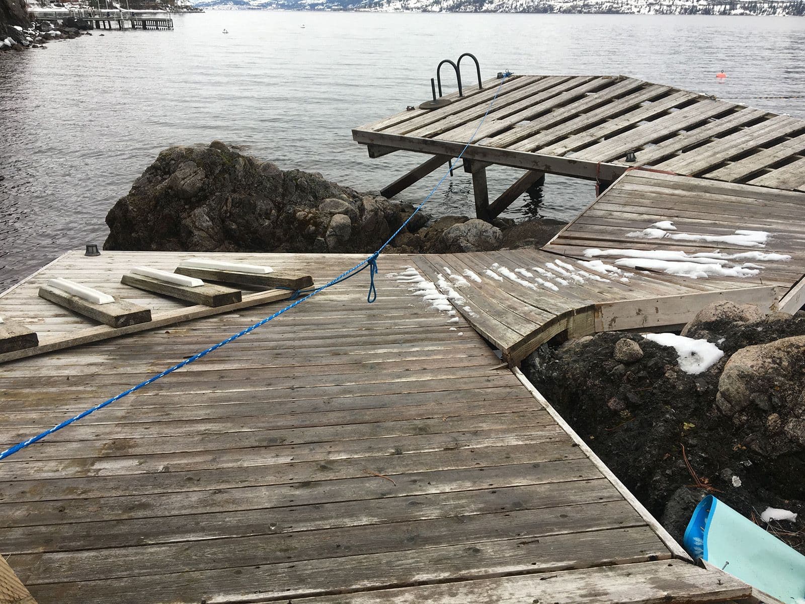 Damaged residential dock with warped wood panels and snow-covered ramps on Okanagan Lake, captured before structural restoration and safety upgrades.
