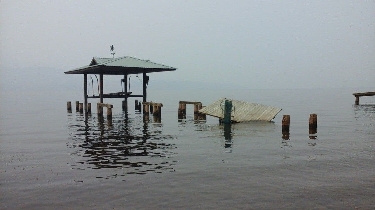 Storm-damaged dock with collapsed decking and exposed pilings on Okanagan Lake, awaiting full restoration after severe structural failure.