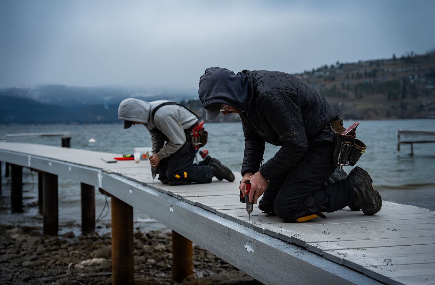 Two dock builders fastening deck boards with power tools, demonstrating high construction standards, attention to detail, and pride in quality workmanship.